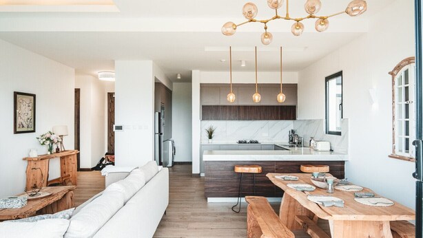 A modern kitchen with a central island, pendant lighting, and a dining area with wooden tables and benches. - Luxury 2BR at Two Rivers | Pool, Gym, UN Zone (Nairobi)