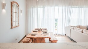 A dining area with a wooden table set for four, a sofa, and a chandelier. - Luxury 2BR at Two Rivers | Pool, Gym, UN Zone (Nairobi)
