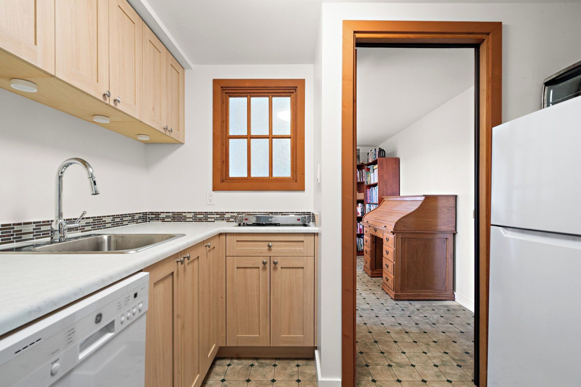 A kitchen with wooden cabinets, a built-in dishwasher, a window, and a tiled backsplash.