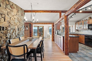 Une cuisine spacieuse avec des poutres en bois, un mur en pierre et un coin repas comprenant une table et des chaises.