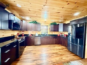 Eine moderne Küche mit Holzbalkendecke, Edelstahlgeräten und dunklen Schränken.