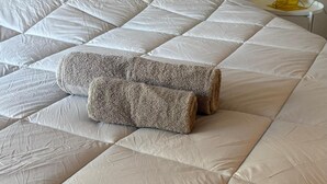 Una cama con un colchón acolchado, una manta enrollada y una lámpara amarilla sobre una mesita de noche.