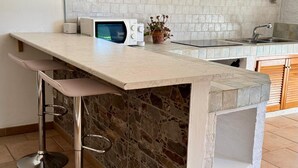 Una cocina con una isla de piedra, taburetes de bar, horno empotrado y salpicadero de azulejos blancos.