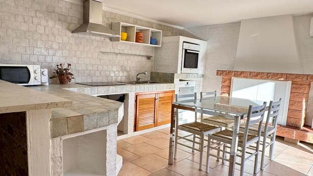 Una cocina con encimera de piedra, microondas, fregadero y zona de comedor con sillas.