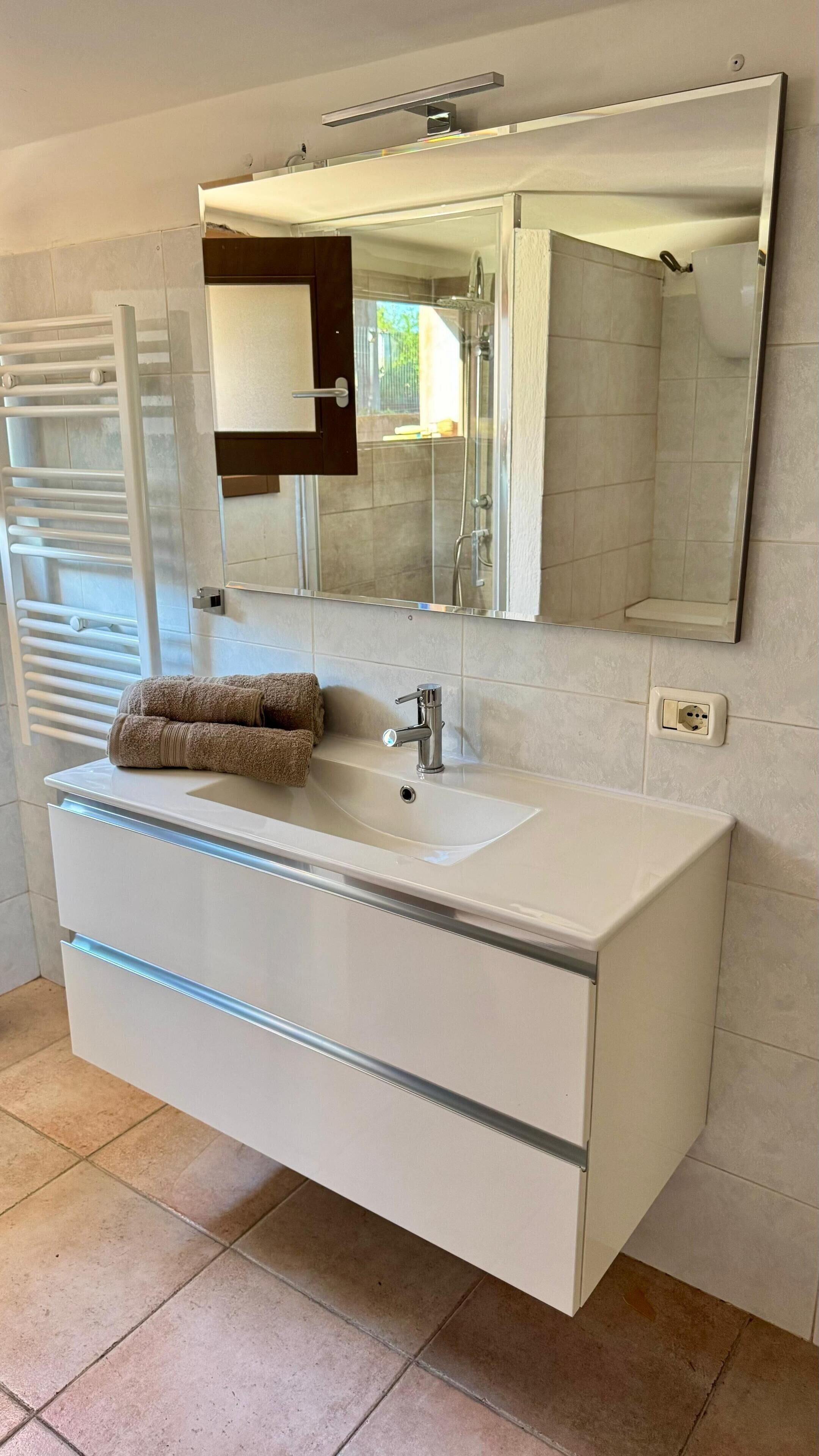 Un baño con tocador blanco, un espejo grande, una toalla y cabina de ducha.