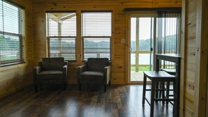 A wooden cabin interior with two armchairs, a small table, and large windows offering a view of the outdoors. - The Duke- Lakehouse at Arc Ridge Ranch Resort (Ben Wheeler)