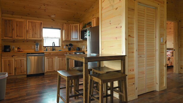 Interno di una baita in legno con cucina, tavolo da pranzo in legno e sedie.