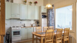 Una cocina con armarios blancos, estufa, microondas y una zona de comedor con sillas de madera y una mesa.