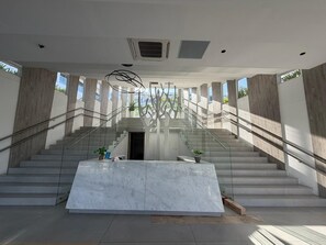 Ein modernes Interieur mit einem Marmor-Empfangstresen, einer Treppe mit Glasgeländern und einer dekorativen Baumskulptur.
