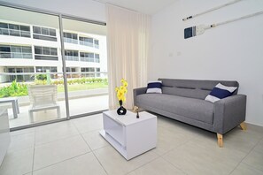 Ein modernes Wohnzimmer mit grauem Sofa, weißem Beistelltisch und Blick auf ein Gebäude durch große Fenster.