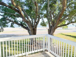 Eine Holzterrasse mit weißen Geländern, die auf einen Strand mit einer Straße und einem weißen Auto in der Ferne blickt.
