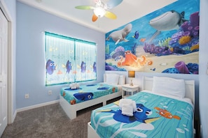 Een kinderkamer met twee bedden, een plafondventilator, een raam met gordijnen en een muurschildering van een onderwaterwereld.