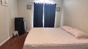 Une chambre à coucher comprenant un lit, un petit bureau, une chaise, une fenêtre avec des rideaux et un luminaire au plafond.
