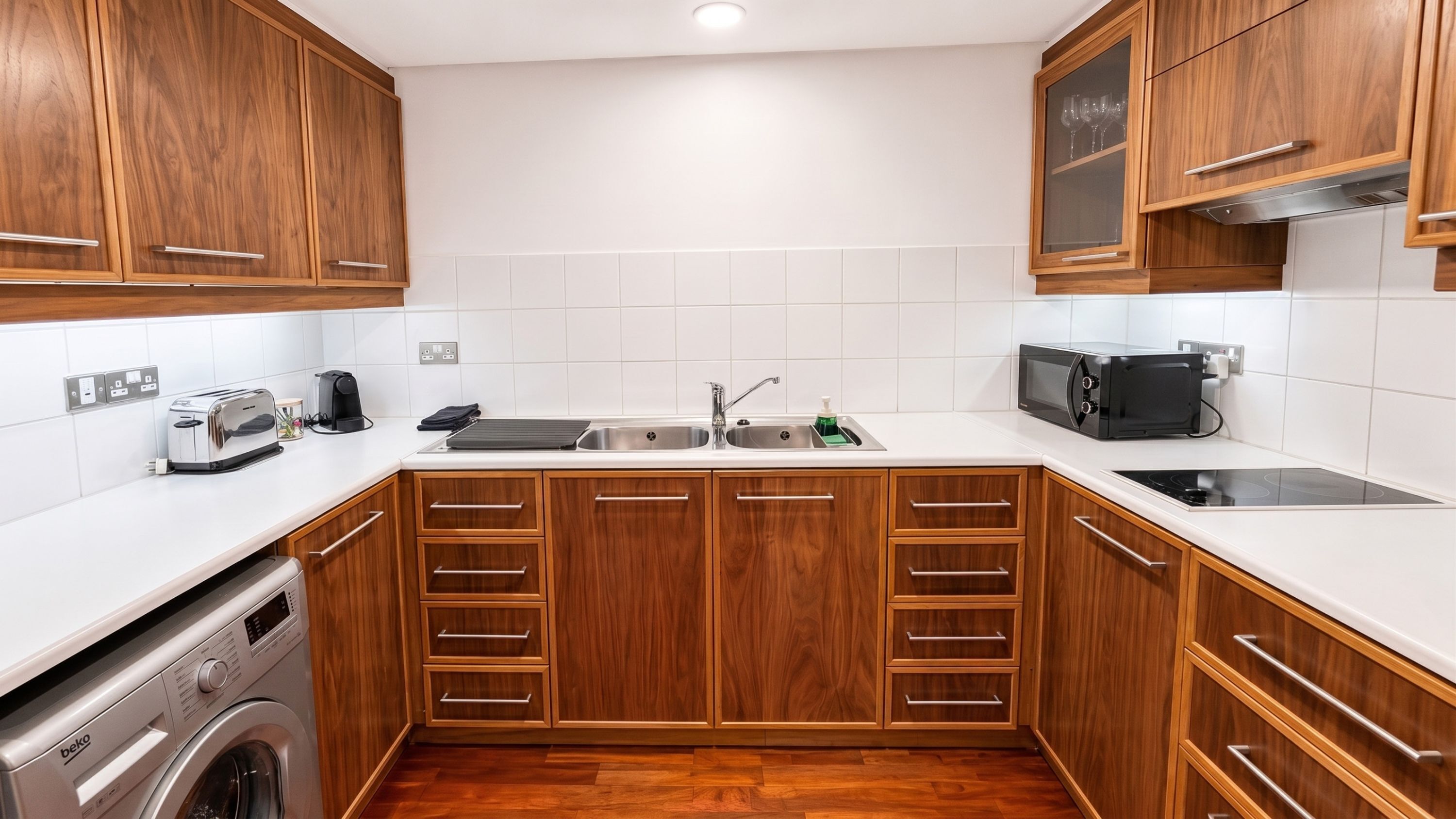 Una cocina moderna con armarios de madera, lavadora integrada, un lavamanos doble y un microondas.