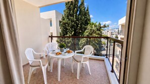 En balkon med et bord dækket til to, stole, en potteplante og udsigt til et træ og bygninger.