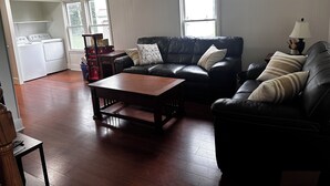 A living room with a black leather sofa, a wooden coffee table, and a laundry area with a washing machine and dryer. - MBC- Cozy home, Direct Access Snowmobile/ATV Trail (Presque Isle)