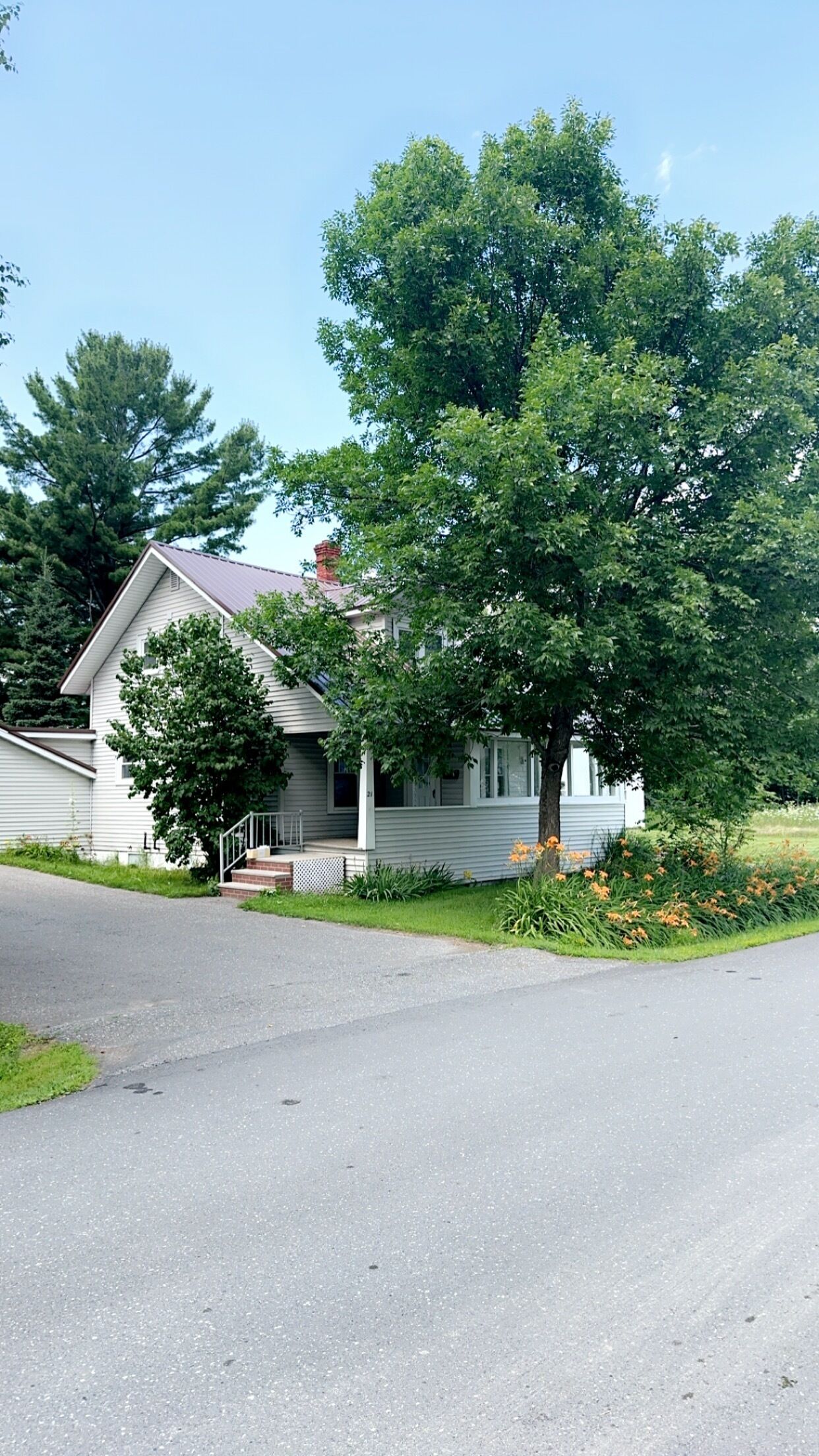 Una casa a un piano con veranda, un camino e un grande albero di fronte.