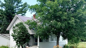 A single-story house with a front porch, a chimney, and a large tree in front. - MBC- Cozy home, Direct Access Snowmobile/ATV Trail (Presque Isle)