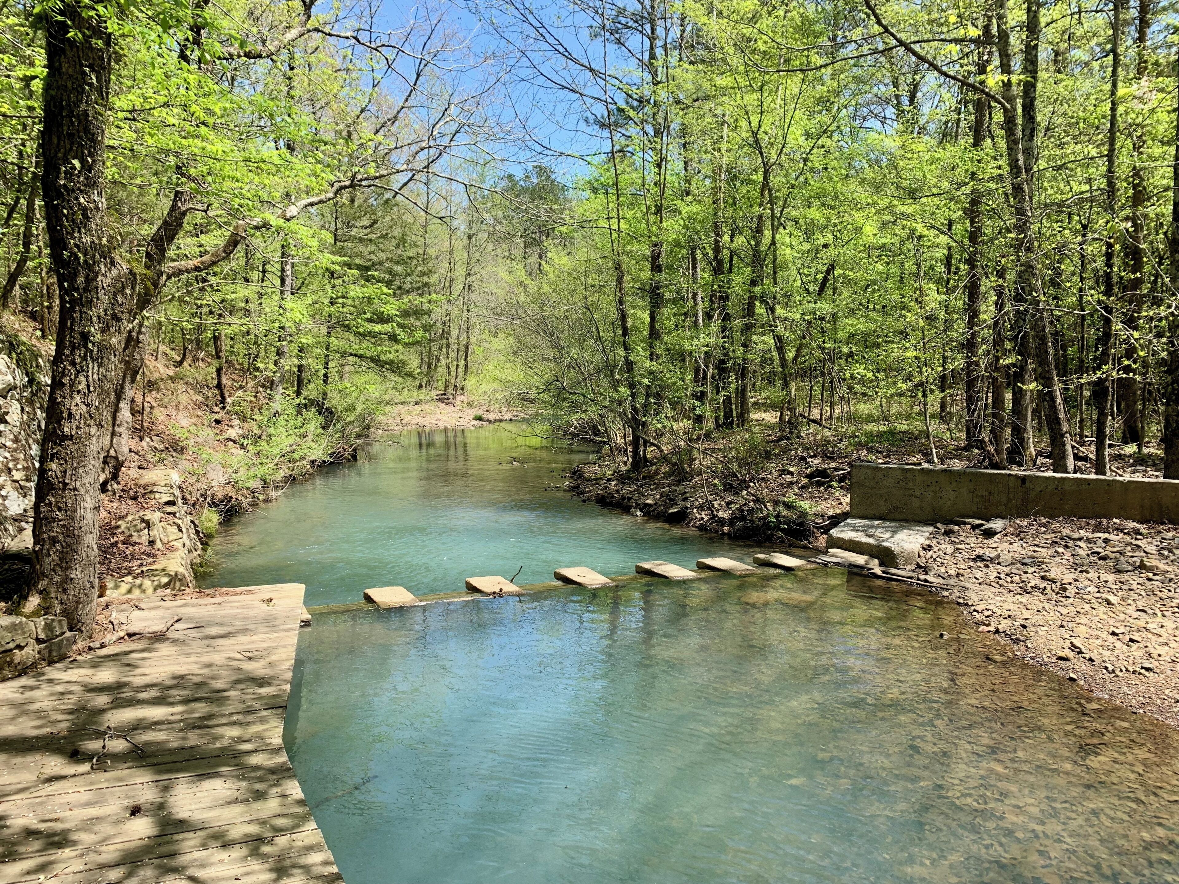 Un río de aguas cristalinas, rodeado de árboles y un puente de hormigón.