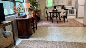 Una cocina con una mesa de comedor, sillas, un televisor, una lámpara, una planta, armarios, un microondas, una estufa y un refrigerador.