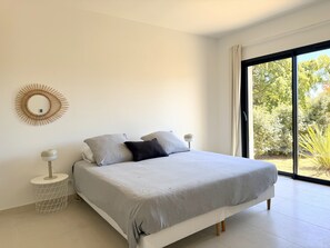 A bedroom with a bed, a round wall decoration, a bedside lamp, and a view of greenery through a large window.