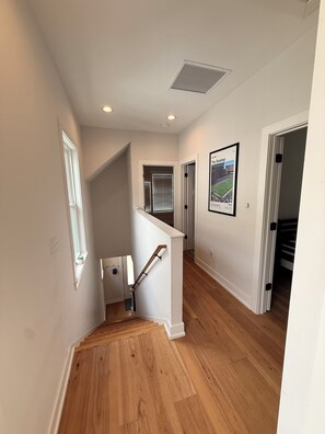 Ein Flur mit Holzboden, weißen Wänden, einer Holztreppe mit Handlauf und einem Deckenventil.