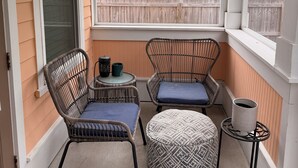 Un porche cubierto con muebles de mimbre, una mesita y vistas a una casa de madera y árboles.