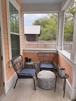 Eine überdachte Veranda mit Korbmöbeln, einem kleinen Tisch und Blick auf ein Holzhaus und Bäume.