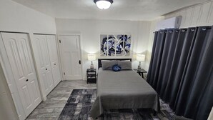 Habitación de hotel con cama, dos mesitas de noche, una obra de arte en la pared, una lámpara de techo y una ventana con cortinas.