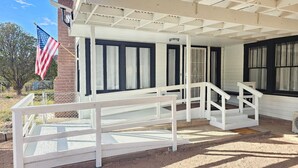 Un porche cubierto con barandal blanco, pared de ladrillo y una bandera estadounidense.