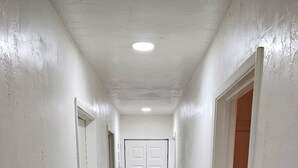 Un pasillo estrecho con paredes blancas, piso de madera y una puerta al final.