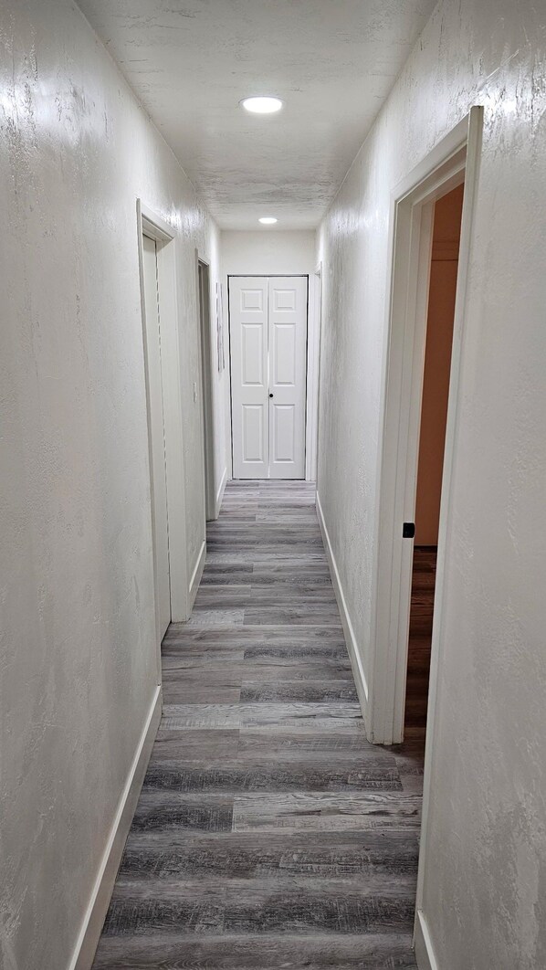 Un pasillo estrecho con paredes blancas, piso de madera y una puerta al final.
