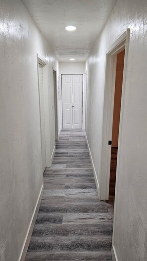 A narrow hallway with white walls, a wooden floor, and a door at the end.