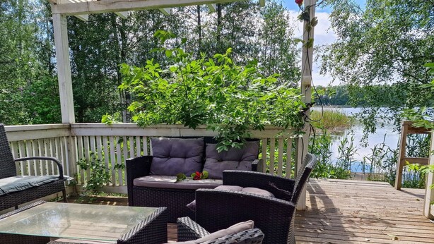 Terraza de madera con mobiliario de mimbre y una mesa de vidrio.