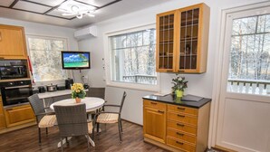 Una cocina con una mesa de comedor, sillas, un televisor, armarios y una ventana con vistas a árboles.