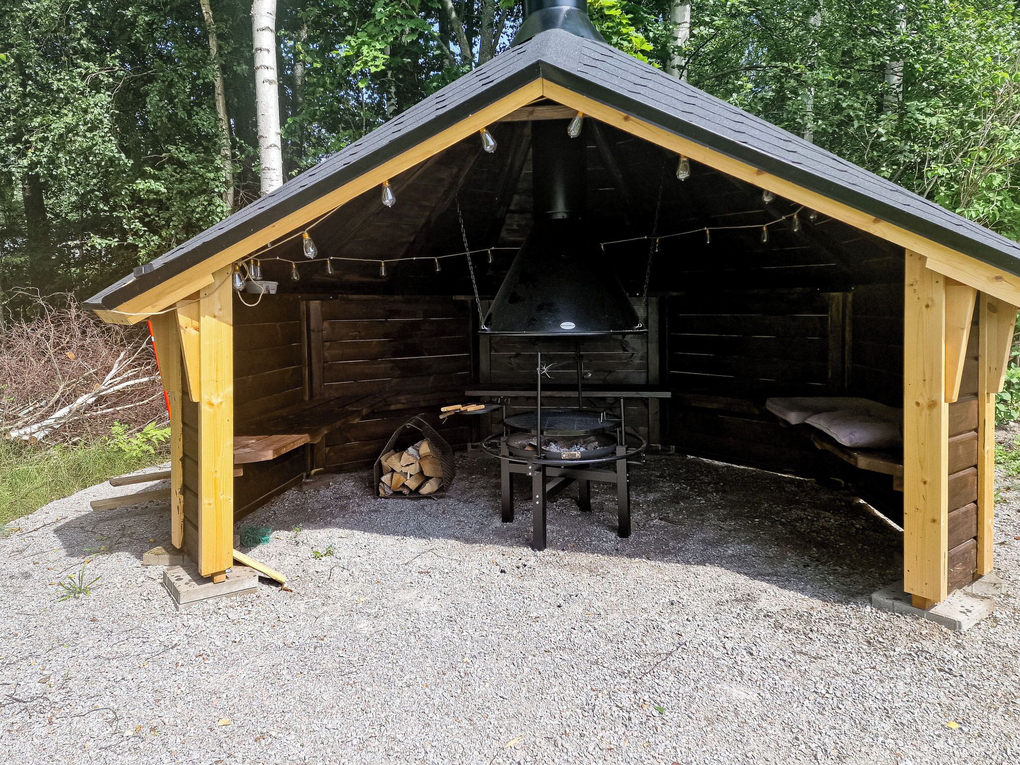 Une structure extérieure en bois, dotée d’une cheminée, d’un barbecue et d’un espace salon.
