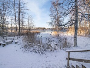 Eine verschneite Landschaft mit einem zugefrorenen See, kahlen Bäumen und einer hölzernen Bank.