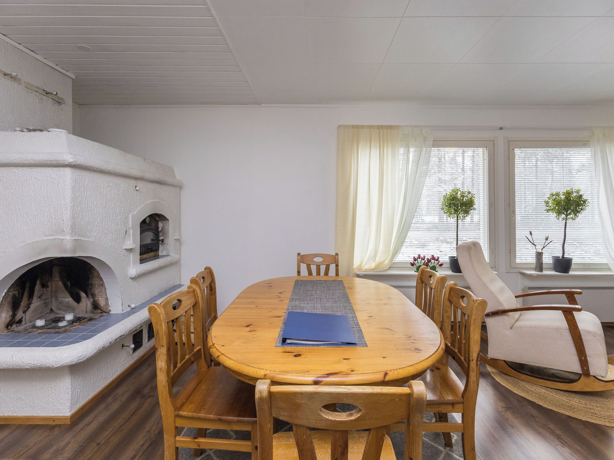Ein gemütliches Zimmer mit Kamin, einem Esstisch und zwei mit Vorhängen versehenen Fenstern.