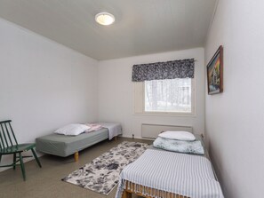 A small, well-lit room with two single beds, a chair, a radiator, and a window with a patterned valance.