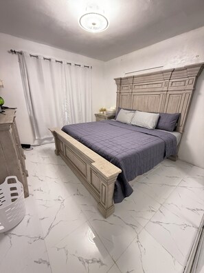 A bedroom with a bed, a nightstand, a dresser, and a marble floor.