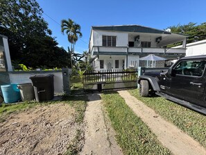 A two-story house with a paved driveway, a black SUV parked in front, and a fenced yard.