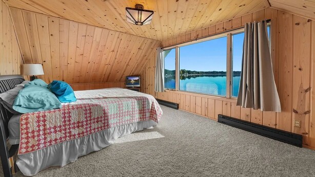 Ein Schlafzimmer mit Bett, Fernseher, einem Fenster mit Vorhängen und Seeblick.