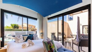 Een moderne hotelkamer met een groot bed, een blauwe bank en een balkon met buitenmeubilair.