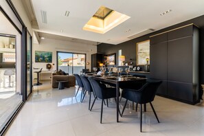 A modern dining area with a long table, black chairs, and a glass partition. - La Badoumba · Heated Pool & Jacuzzi (Saleilles)