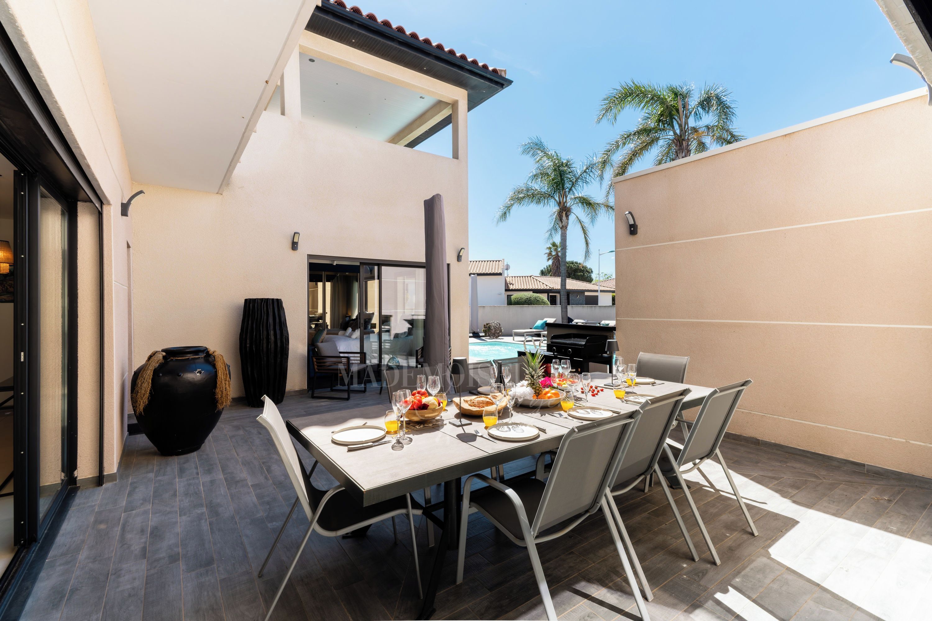 An outdoor dining area with a table set for a meal, a grill, and a pool in the background.