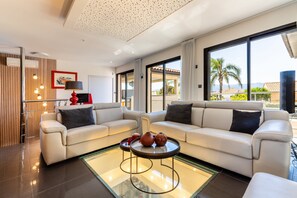 A modern living room with a sofa set, a glass coffee table, and a view of the outdoors. - La Badoumba · Heated Pool & Jacuzzi (Saleilles)