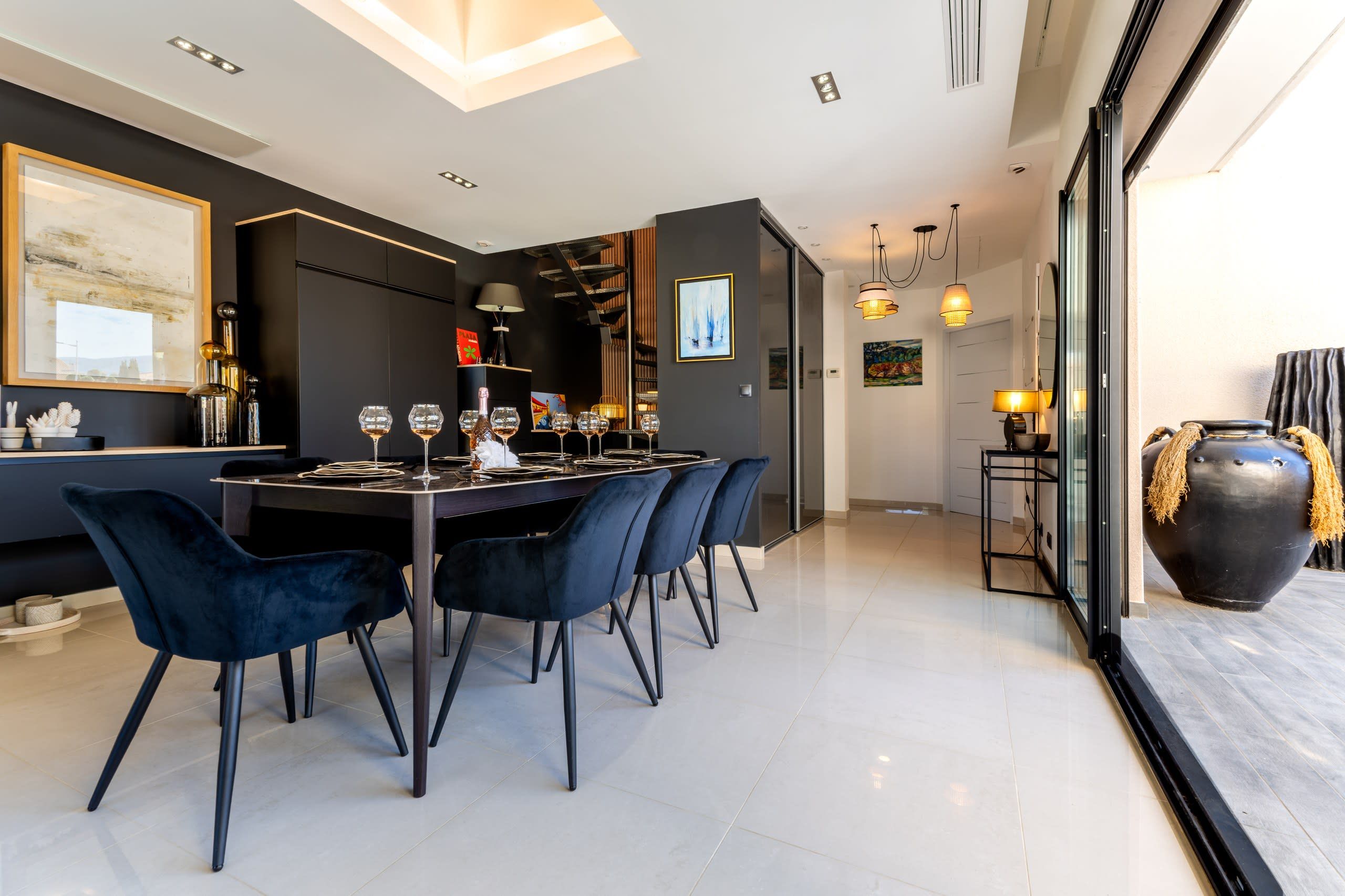 A modern dining area with a long table, dark chairs, and a variety of wine glasses and bottles.