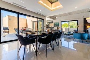 A spacious dining area with a long table, black chairs, and a view of the outside. - La Badoumba · Heated Pool & Jacuzzi (Saleilles)