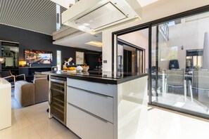 A modern kitchen with a large island, a built-in oven, and a glass door refrigerator. - La Badoumba · Heated Pool & Jacuzzi (Saleilles)