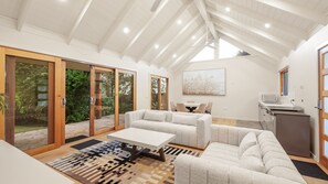 A modern living room with a high ceiling, sliding glass doors to a garden, a dining area, and a kitchenette. - Seaview Escape in Ventnor (Ventnor)